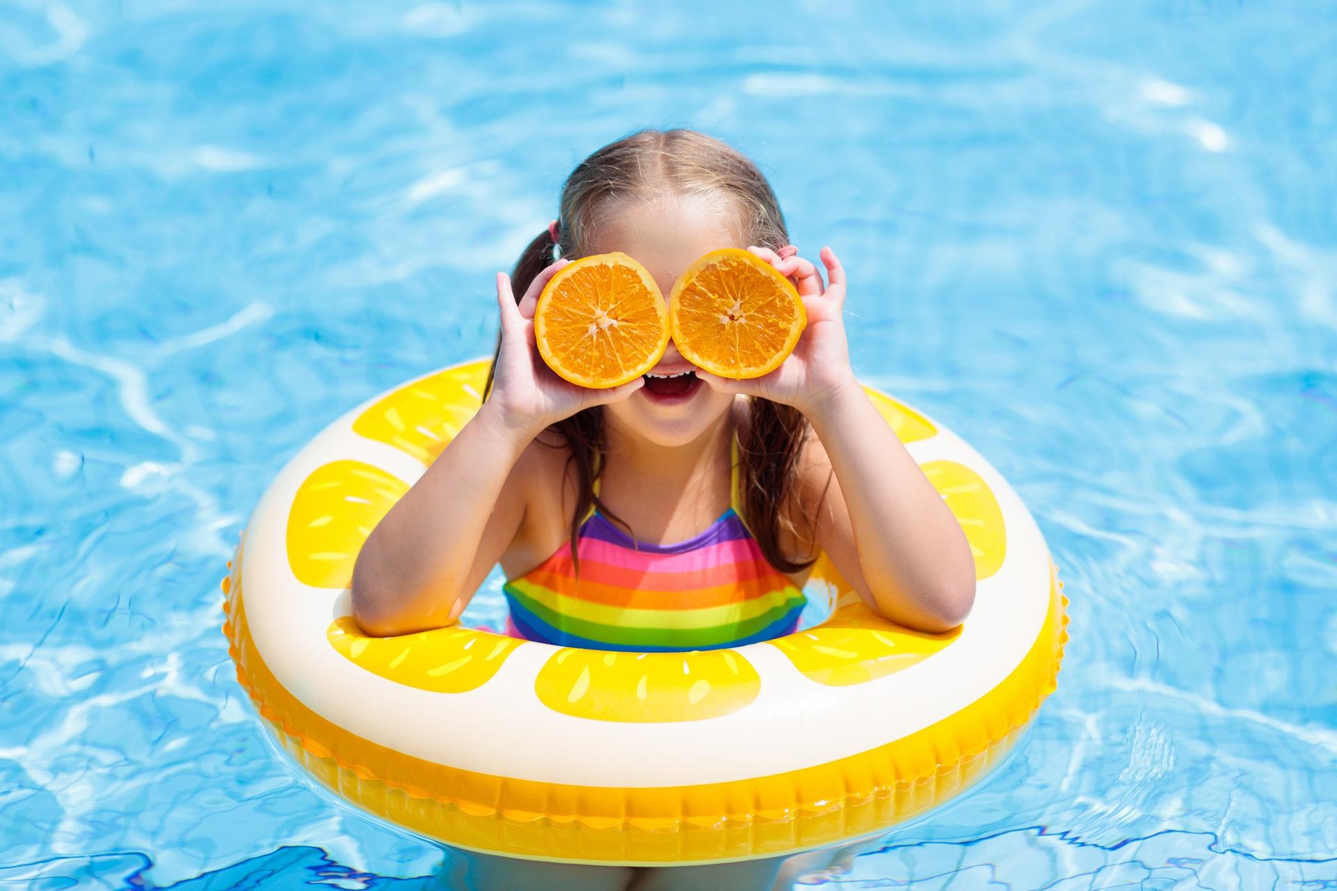 Kind im Pool hält Orangenhälften vor die Augen | Ferienbetreuung